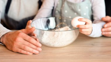 Baba ve kızı mutfakta hamuru birlikte hazırlıyorlar, evde hamur işi pişirirken yumurta ekliyorlar, kırpılmış resim, yakın plan.