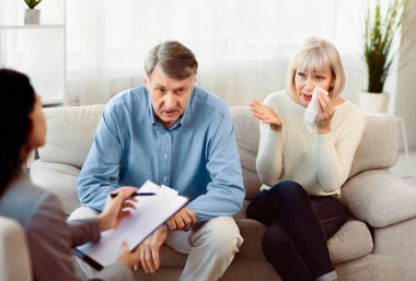 Evlilik danışmanlığı. Yaşlı çift koltukta oturup psikologla konuşuyor, doktor notlar alıyor, kadın ağlıyor.
