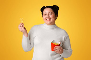 Causes Of Weight Gain. Portrait Of Happy Millennial Plump Woman Eating French Fries, Enjoying Junk Food, Standing Over Yellow Background, Panorama