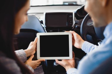 Couple Using Digital Tablet With Empty Screen Sitting In New Car In Dealership Center. Mockup, Back View, Selective Focus