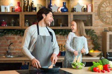 Mutlu baba ve küçük kız birlikte yemek pişirirken gülüyorlar, mutfakta eğleniyorlar, hamuru kaseye karıştırıyorlar..