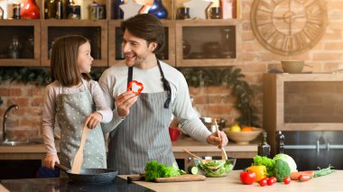 Yemek zamanı. Neşeli genç baba ve küçük kızı mutfakta öğle yemeği hazırlıyorlar, karantina sırasında eğleniyorlar, evde kalmaktan keyif alıyorlar.