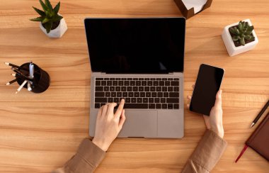 Top View Of Office Workplace. Female manager sitting at wooden desk, using laptop and smartphone, mock up, flatlay, copyspace