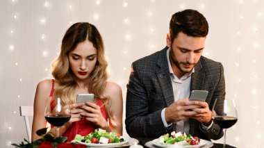 Sosyal medya bağımlılığı konsepti. Romantik bir buluşmada akıllı telefonlarıyla vakit geçiren çiftler birbirlerini görmezden geliyorlar.