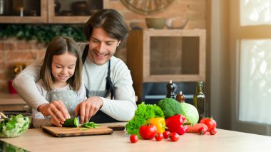 Aile yemekleri. Önemseyen bir baba küçük kızına yemek yapmayı öğretiyor, salatalığı bıçakla doğruyor, birlikte kesiyorlar, boş alan yaratıyorlar.