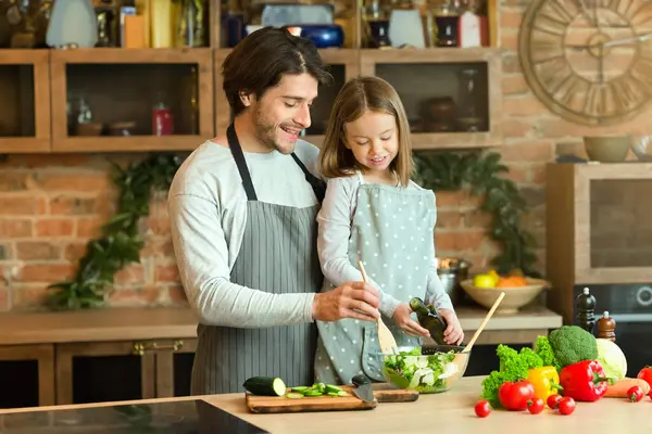 Neşeli küçük baba ve küçük kız mutfakta birlikte sağlıklı salata hazırlıyorlar, karınca yuvası pişiriyorlar, bedava yer açıyorlar.