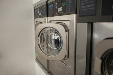 Bir dizi gösterişli, paslanmaz çelik çamaşır makinesi öğleden sonra bir self-servis çamaşırhanesinde çalışır ve müşteriler için temiz ve verimli bir yıkama deneyimi sunar..