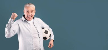 - Devam et. Heyecanlı orta yaşlı bir adam mavi atölye duvarında futbol topuyla kazanan jest yapıyor.