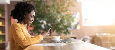 Güzel afro kız kahve içiyor, çalışıyor ve akıllı telefon kullanıyor, kafenin içi, fotokopi odası, yan görüş