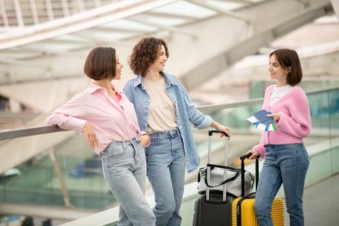 Three friends chat and laugh together at an airport terminal while preparing for their upcoming trip. They hold travel documents and stand near their luggage in a lively environment. clipart