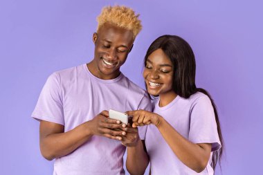 Mutlu siyahi kadın ve erkek menekşe arka planında cep telefonu kullanıyor.