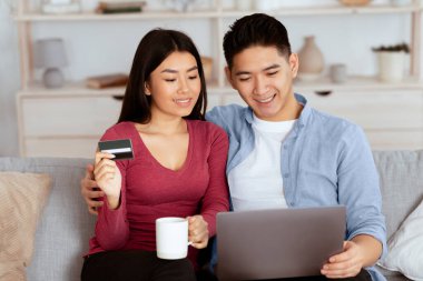 İnternetten alışveriş. Çinli çift hafta sonu evdeki koltukta dizüstü bilgisayar ve kredi kartı kullanıyor.