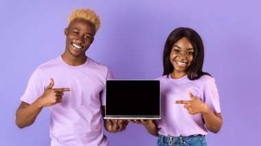 Milenyum Afrikalı Amerikalı kadın ve erkek boş dizüstü bilgisayarı işaret ediyor. Leylak arkaplan, web sitesi tasarımın için alan. Panorama