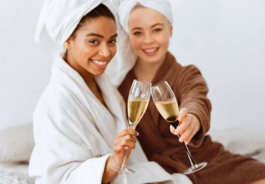 Bornozlu gülümseyen çok ırklı kız arkadaşlar evde spa gününü kutluyorlar, kapatıyorlar.