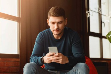 Millennial Guy, Modern Daire İçi 'nde, Fasulye Koltuğu' nda oturan akıllı telefon mesajları kullanıyor. Seçici Odaklanma
