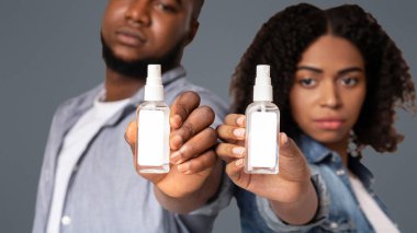 Beyaz etiketli dezenfektan spreyleri hafif arka planda duran, seçici odaklı genç Afrikalı Amerikalı bir çiftin ellerinde.