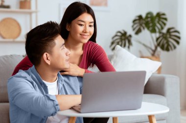 Tatil planlama. Şirin Asyalı çift oteli ve tatil köyünü arıyor, evde dizüstü bilgisayar kullanıyorlar, boş yer var.