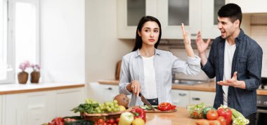 Aile sorunları kavramı. Genç bir çift mutfakta tartışıyor, adam bağırıyor, kadın onu durduruyor, avuç içini gösteriyor.