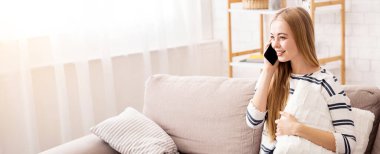Gülümseyen genç bayan akıllı telefonda konuşuyor, evdeki kanepede dinleniyor, boş yeri olan bir panorama.