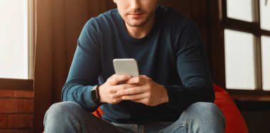 Unrecognizable Guy Using Mobile Phone Playing Games Sitting In Beanbag Chair Indoor. Panorama, Cropped, Selective Focus