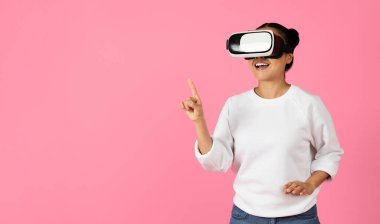 Sanal gerçeklik kulaklığı takan bir kadın dijital dünyayla etkileşime girerken gülümsüyor. Tek eliyle hareket ediyor, belli ki meşgul ve deneyimi için heyecanlı..