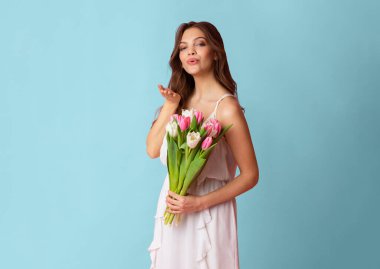 Çekici genç bayan lale buketi tutuyor ve stüdyoda renkli bir arka plan pozu verirken kameraya hava öpücüğü yolluyor.