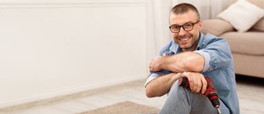 Olgun Adam mobilya montajı elektrikli matkapla oturma pozu evde kameraya gülümsüyor. Marangozluk Konsepti