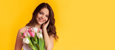 Güzel gülümseyen bir kadının portresi. Renkli arka planda duran bir buket lale ve boş alan.