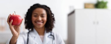Afrikalı kadın doktor elinde kırmızı taze elma, seçici odaklanma, sağlıklı gıda konsepti