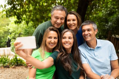 Beş kişilik bir grup, güneşli bir günde yemyeşil bir ortamda, bir parkta toplanır, gülümser ve eğlenceli bir selfie için poz verirler. Mutlulukları arkadaşlığın özünü yansıtır..