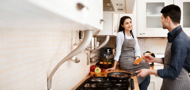 Birlikte yemek pişirmek. Mutlu çift yemek hazırlıyor, tavada kızarıyor, birbirine bakıyor, kız tezgahta oturuyor.
