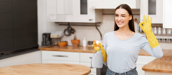 Keeping Your House Clean. Smiling woman wearing yellow rubber gloves showing ok sign, holding spray, copy space