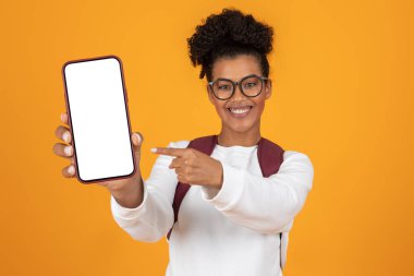 Kıvırcık saçlı neşeli genç bir kadın, boş ekrana işaret eden bir akıllı telefonu önünde tutuyor. Parlak turuncu arka plan sahneye enerji katıyor ve canlı bir atmosfer yaratıyor..