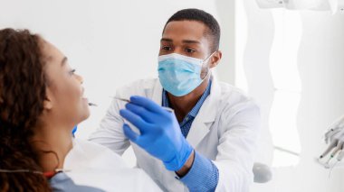 Siyahi bir stomatolog klinikte genç bayanların dişlerini kontrol ediyor.