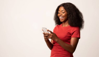 Arkadaşlarıyla mesajlaşmak için akıllı telefon kullanan neşeli siyahi kadının portresi, Beyaz Stüdyo Arkaplanı 'nın başında dikilirken cep telefonuyla mesajlaşan mutlu Afrikalı Amerikalı bayan,