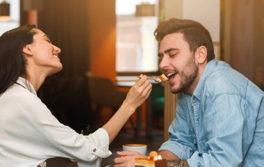 Loving Couple Feeding Each Other Tasting Dessert And Coffee On Romantic Date Sitting In Cafe. Dating And Relationship