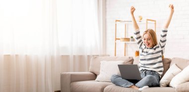 Happy blonde girl celebrating success, got dream job, using laptop at home, copy space