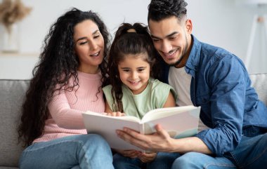 Genç Arap ebeveynler evde tatlı küçük kızlarıyla kitap okuyorlar, mutlu bir Orta Doğulu aile oturma odasında oturuyor, ev işlerinin keyfini çıkarıyor ve birlikte vakit geçiriyorlar.