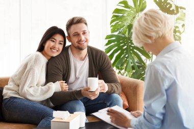 Adoption Counseling. Cheerful Young Couple Talking With Family Psychologist Sitting On Couch In Office. Selective Focus clipart