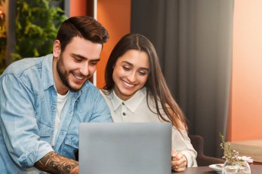 Modern romantizm. Neşeli Aşıklar Romantik Randevu sırasında Konforlu Kafeteryada Oturan Dizüstü Bilgisayarı Kullanıyor