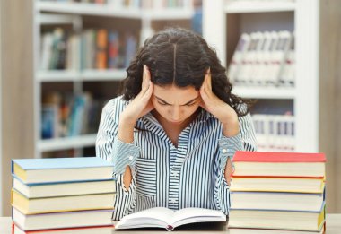 Stress. Tired young mexican student reading book preparing for exam in library at university, trying to focus, copyspace