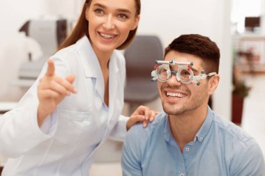 Göz Testi Konsepti. Güzel bayan optometrist hasta görüşünü test çerçevesiyle kontrol ediyor, grafiğe işaret ediyor.