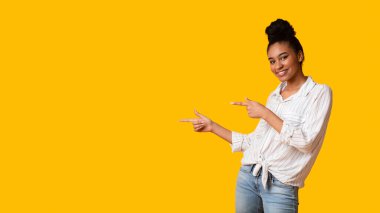 İki parmaklı ve Panorama 'daki kameraya bakan Afro Kız, sarı arka plan üzerinde boşluğu işaret ediyor.