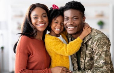 Portrait Of Happy Military Family, Black Soldier Father, Wife And Little Daughter Embracing Together At Home, Cheerful African American Man In Camouflage Uniform Hugging With Spouse And Female Child