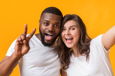 Çift selfie. Neşeli kız afro erkek arkadaşıyla fotoğraf çekiyor, ırklar arası sevgililer kendi portresini çekiyor, sarı arka planda poz veriyor.