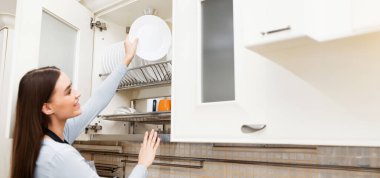 Mutfak Deposu. Tatmin olmuş bir kızın portresi masayı hazırlamak için temiz tabakları dışarı çıkarıyor.