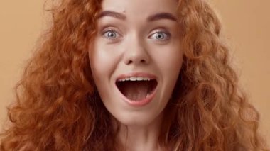 Neşeli genç bir kadın kıvırcık kızıl saçlarını ve geniş gülümsemesini sergiliyor, mutluluk saçıyor. Animasyon ifadesi ve parlak gözleri, sıcak bir ortamda canlandırıcı bir ruh hali sergiliyor..