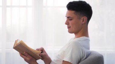 Genç bir adam ışıkla dolu bir odada rahatça oturur, bir kitaba dalmıştır. Pencereden süzülen güneş ışığı sıcak ve huzurlu bir atmosfer yaratıyor. Okumak için mükemmel..