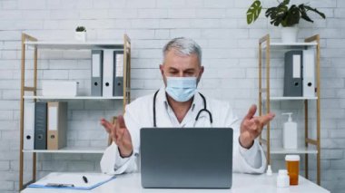 Laboratuvar önlüğü ve maskesi takmış bir sağlık uzmanı sanal danışmanlık yapıyor. Bilgisayarlı bir masada oturmuş, sağlık konularını tartışıyor ve klinik bir ortamda notlar alıyor..