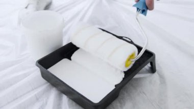 Birisi tepsiden beyaz boya sürmek için boya silindiri kullanırken alan koruyucu plastikle kaplanmış. Çalışma alanı bir ev geliştirme projesi için düzenlenmiştir..